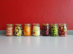 A colourful row of glass mason jars filled with fermented vegetables against a red wall